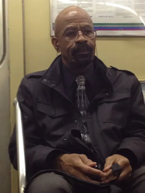 Middle-aged man wearing glasses and formal clothing sitting on public transport.