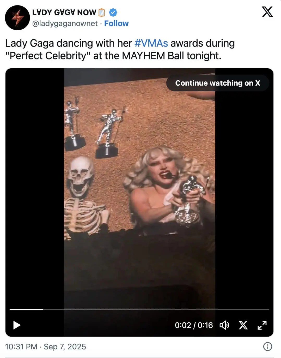 Concert screen shows a blond pop star gleefully shaking a silver VMA “moon person” beside a grinning skeleton prop.