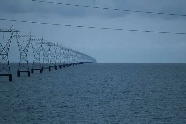 A creepy liminal space showing power lines extending endlessly into the open ocean water.