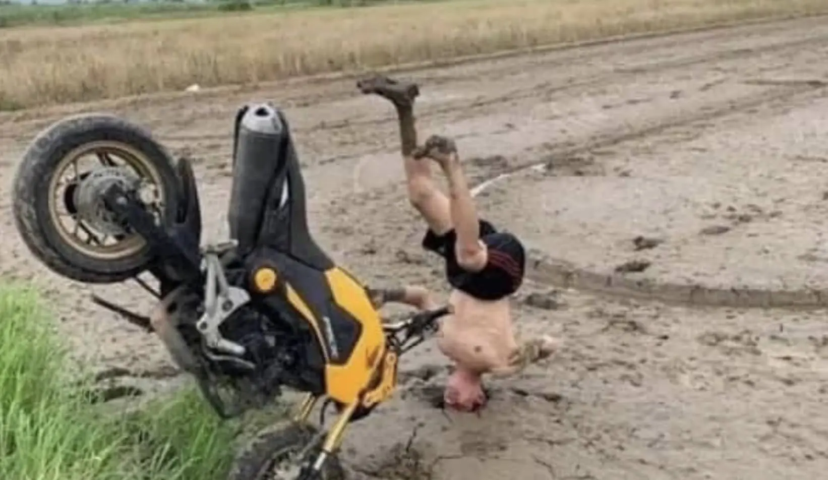 A yellow and black motorcycle stuck upright in mud with a rider's head buried in the ground.
