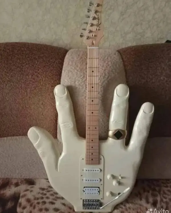 Custom white electric guitar with a body shaped like a large hand wearing a gold ring.