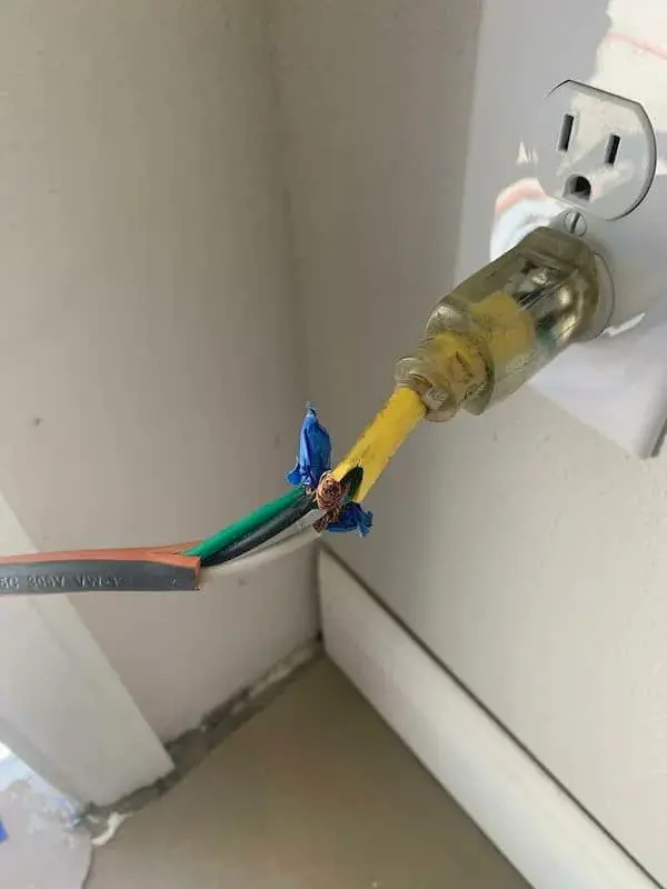 A "fire hazard 101" funny Osha violation picture of an electrical cord where the yellow jacket is torn open, revealing exposed copper wires crudely twisted together and "secured" with a single, tiny piece of blue electrical tape.