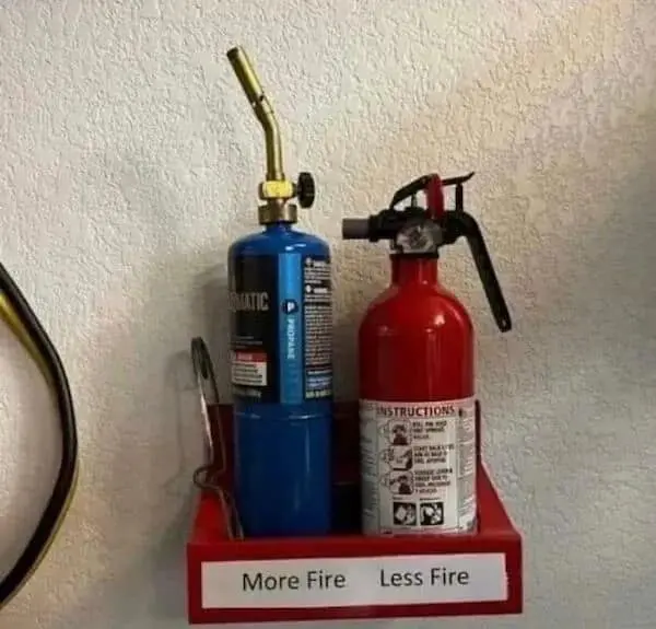 A high-contrast funny osha violation picture showing a blue propane torch and a red fire extinguisher side-by-side on a shelf, helpfully labeled "More Fire" and "Less Fire" respectively.