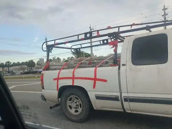 A budget-friendly funny Osha violation picture showing a white pickup truck with a load secured not by ratchet straps, but by several layers of red duct tape wrapped over the top and taped to the side panels in a hopeful grid pattern.