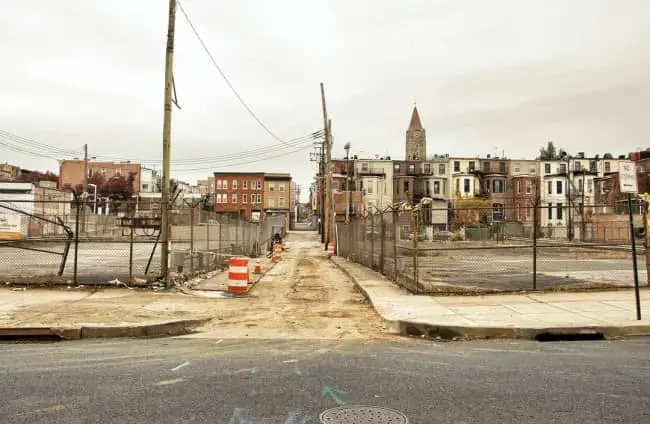 Blighted urban street with empty chain-link lots orange construction barriers and decaying rowhouses