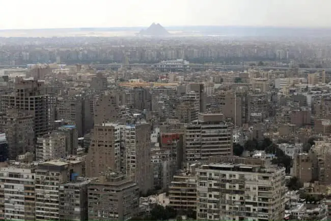 Cairo concrete urban sprawl aerial view with ancient Giza pyramids barely visible through thick haze