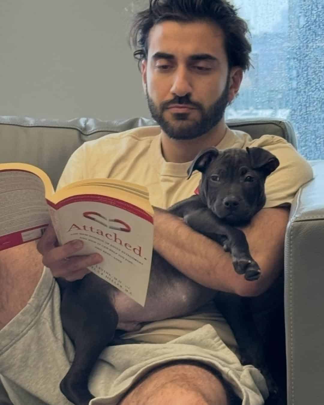 Bearded man reading a relationship book while cuddling puppy