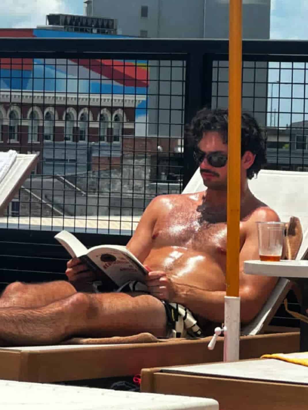 Shirtless man sunbathing and reading by rooftop pool