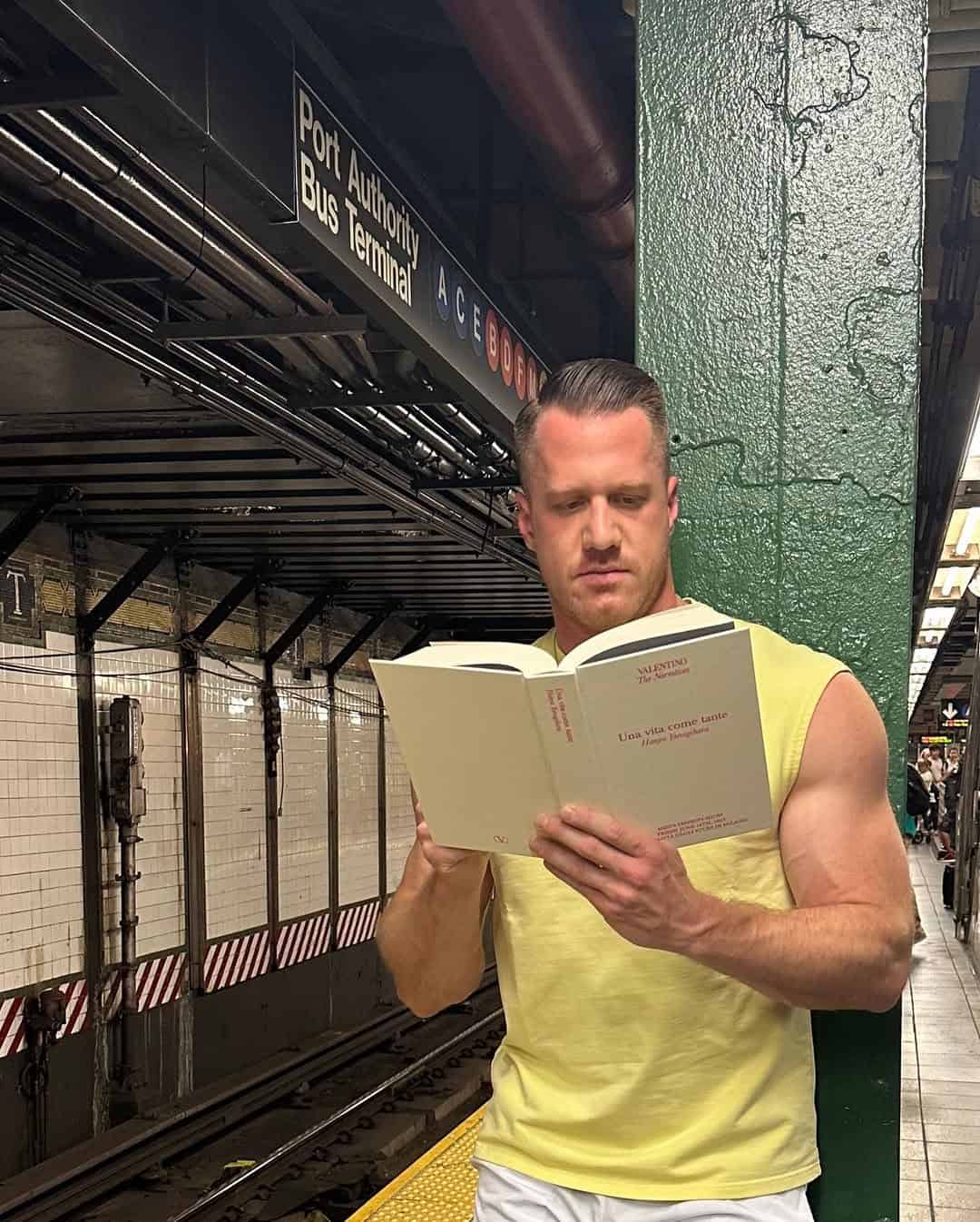 Man reading a book on subway platform in sleeveless shirt