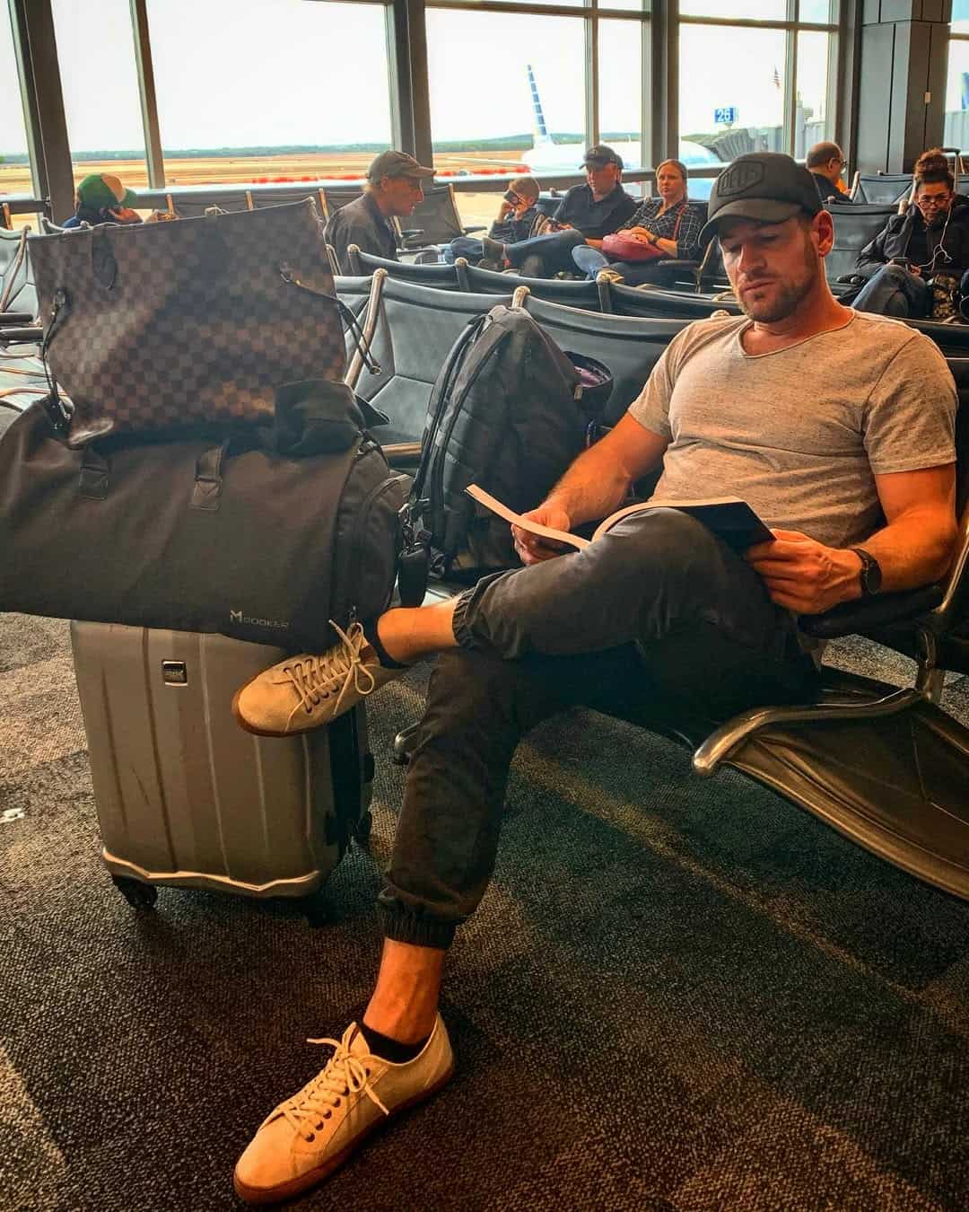 Man sitting at airport gate reading book beside luggage