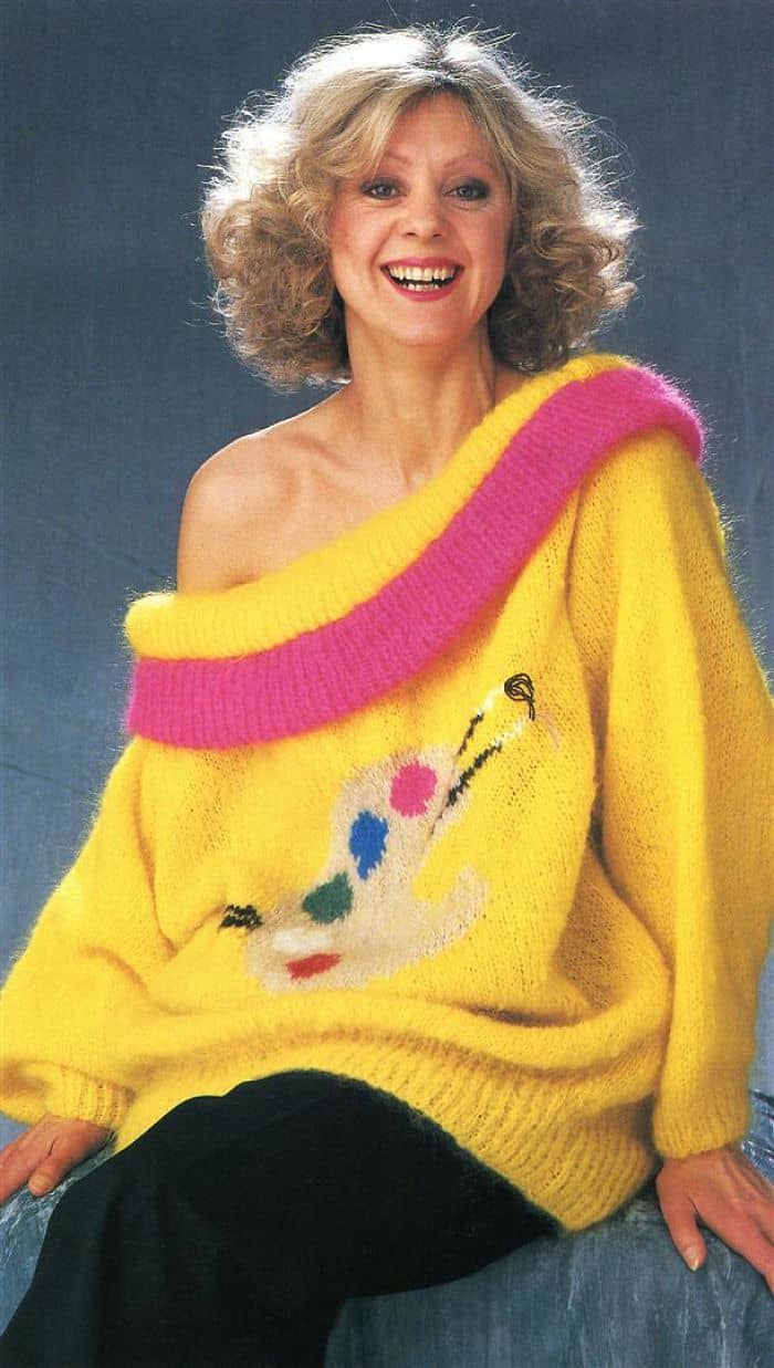 A smiling woman wears an off-the-shoulder fuzzy yellow sweater with a pink neckline and an abstract artist palette graphic.