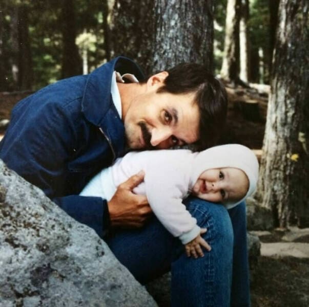 Dad holding baby in a forest while resting heads together and smiling