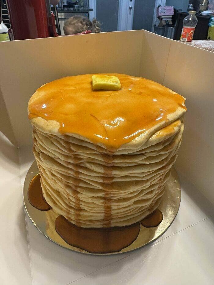 Giant pancake-stack illusion cake with syrup drips and a pat of butter on top.
