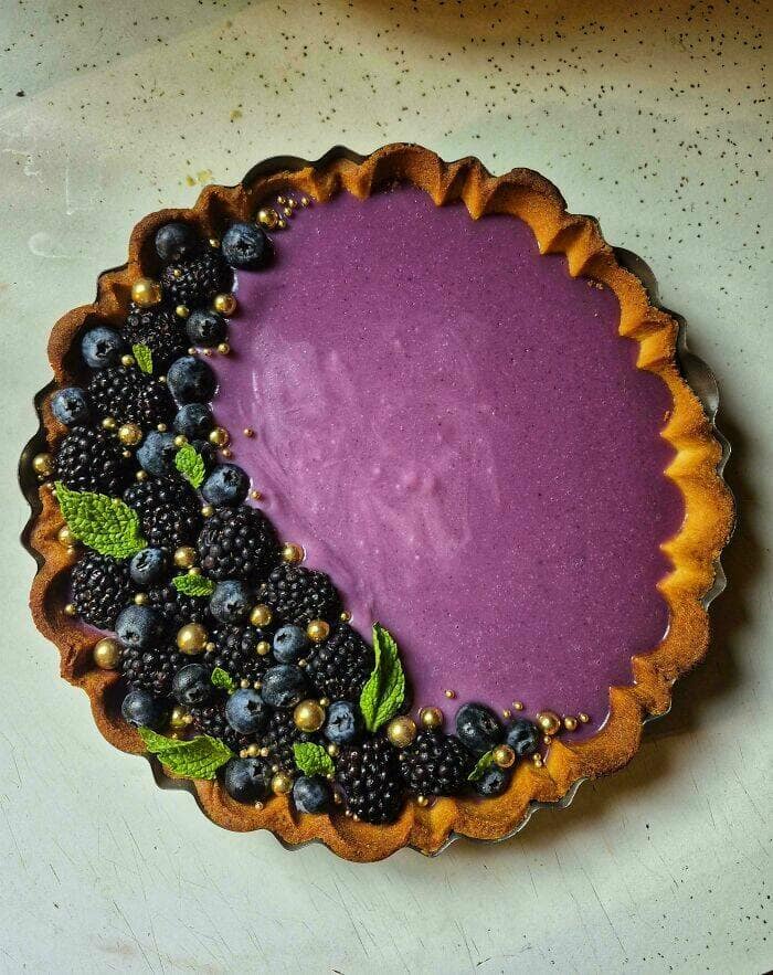 Violet mousse tart with blueberries, blackberries, mint, and gold pearls along the edge.