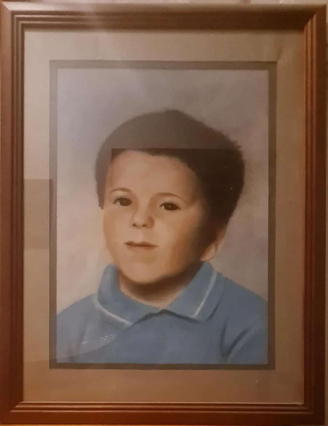 Framed pastel painting of a boy in a blue collared shirt, slightly uncanny proportions behind glass.