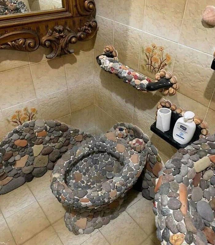 A bathroom toilet, lid, and fixtures completely covered in rough, uncomfortable-looking pebbles.