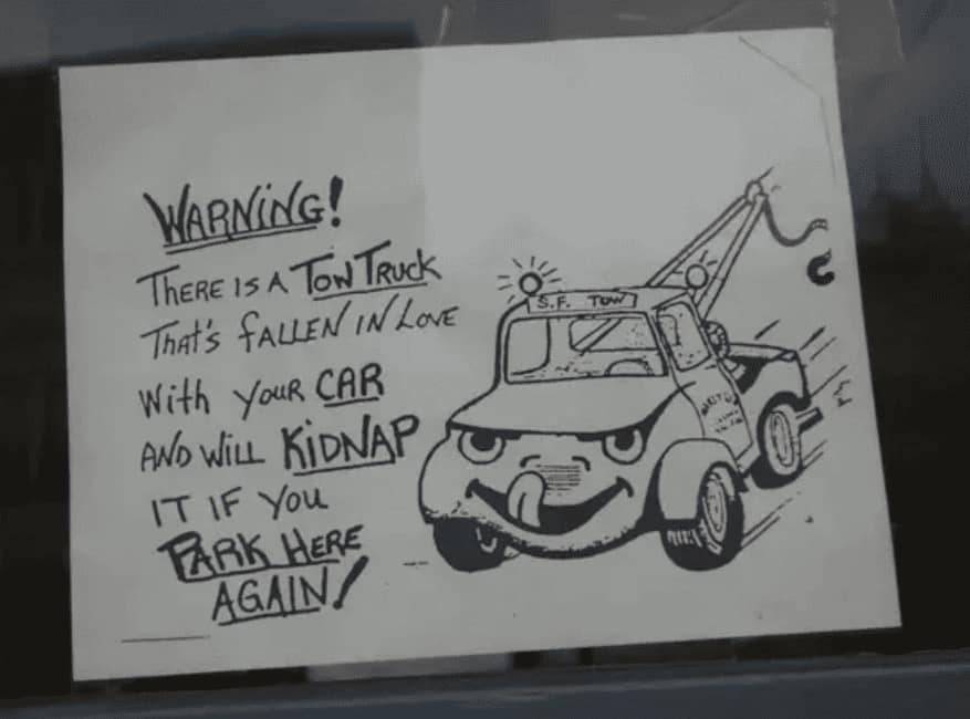 Hand-drawn warning note says a tow truck is “in love” with your car and will “kidnap” it if you park here again.