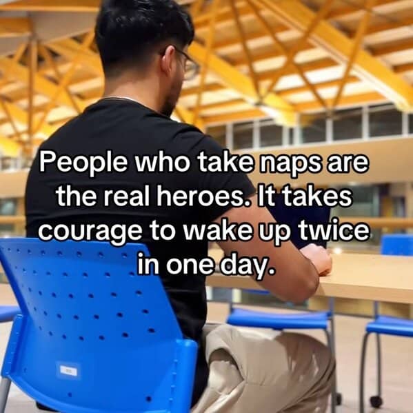 A man in a black shirt sits at a desk in a brightly lit room with the caption: “People who take naps are the real heroes. It takes courage to wake up twice in one day.”