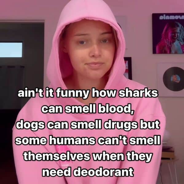 A woman in a pink hoodie gives a deadpan look, with the caption: “ain’t it funny how sharks can smell blood, dogs can smell drugs but some humans can’t smell themselves when they need deodorant.”