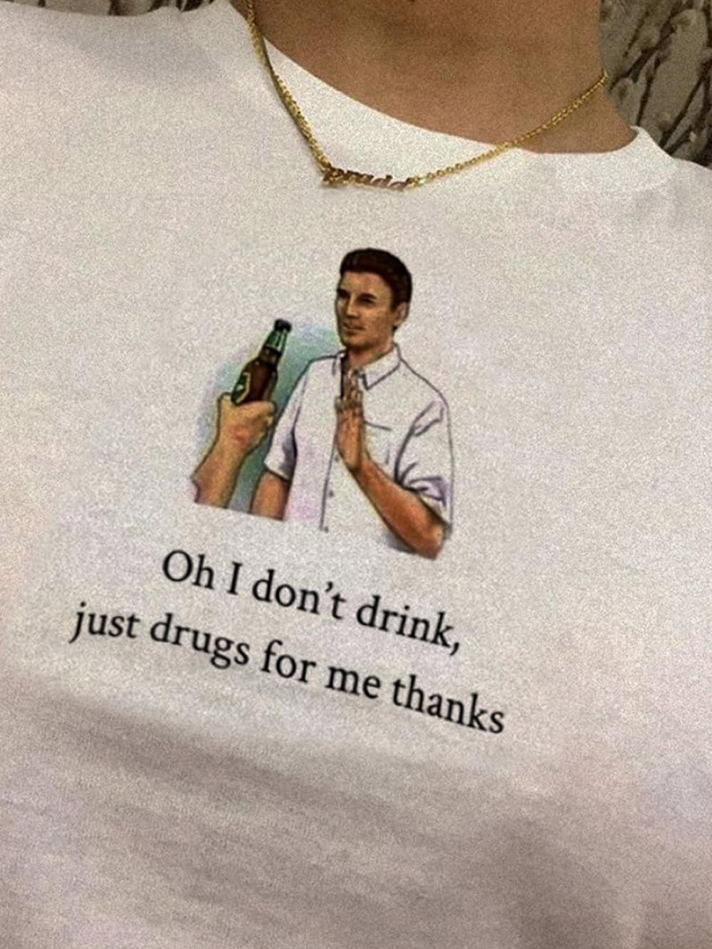 A close-up photo of a white t-shirt with a graphic of a man refusing a drink. Caption below reads: “Oh I don’t drink, just drugs for me thanks.” The combination of vintage clip-art style and the punchline creates awkwardly dark humor.