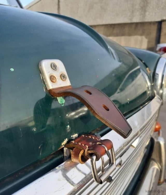 A car hood held down by a belt, fastened with screws, showcasing redneck ingenuity.