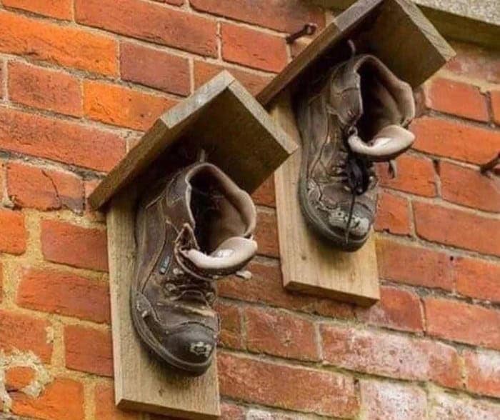 Two old boots turned upside down and nailed to a brick wall, used as birdhouses in a display of redneck ingenuity.