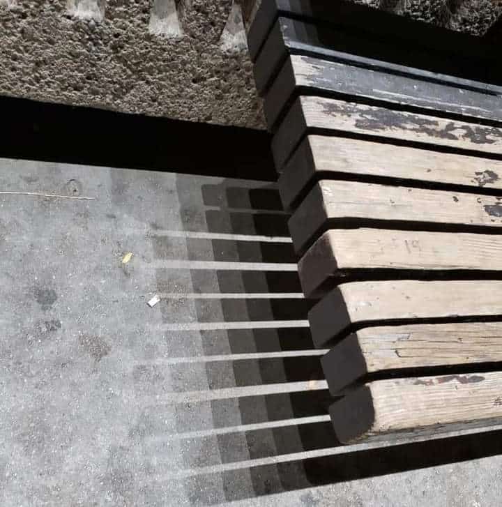 Bench slats casting evenly spaced shadows across concrete