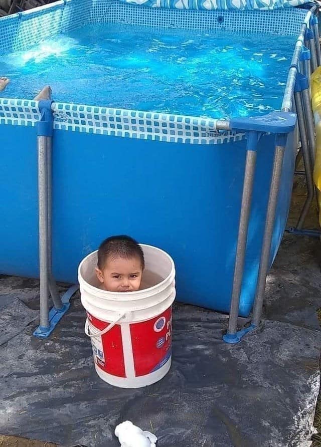 Child sitting in a paint bucket next to a full-sized above-ground pool