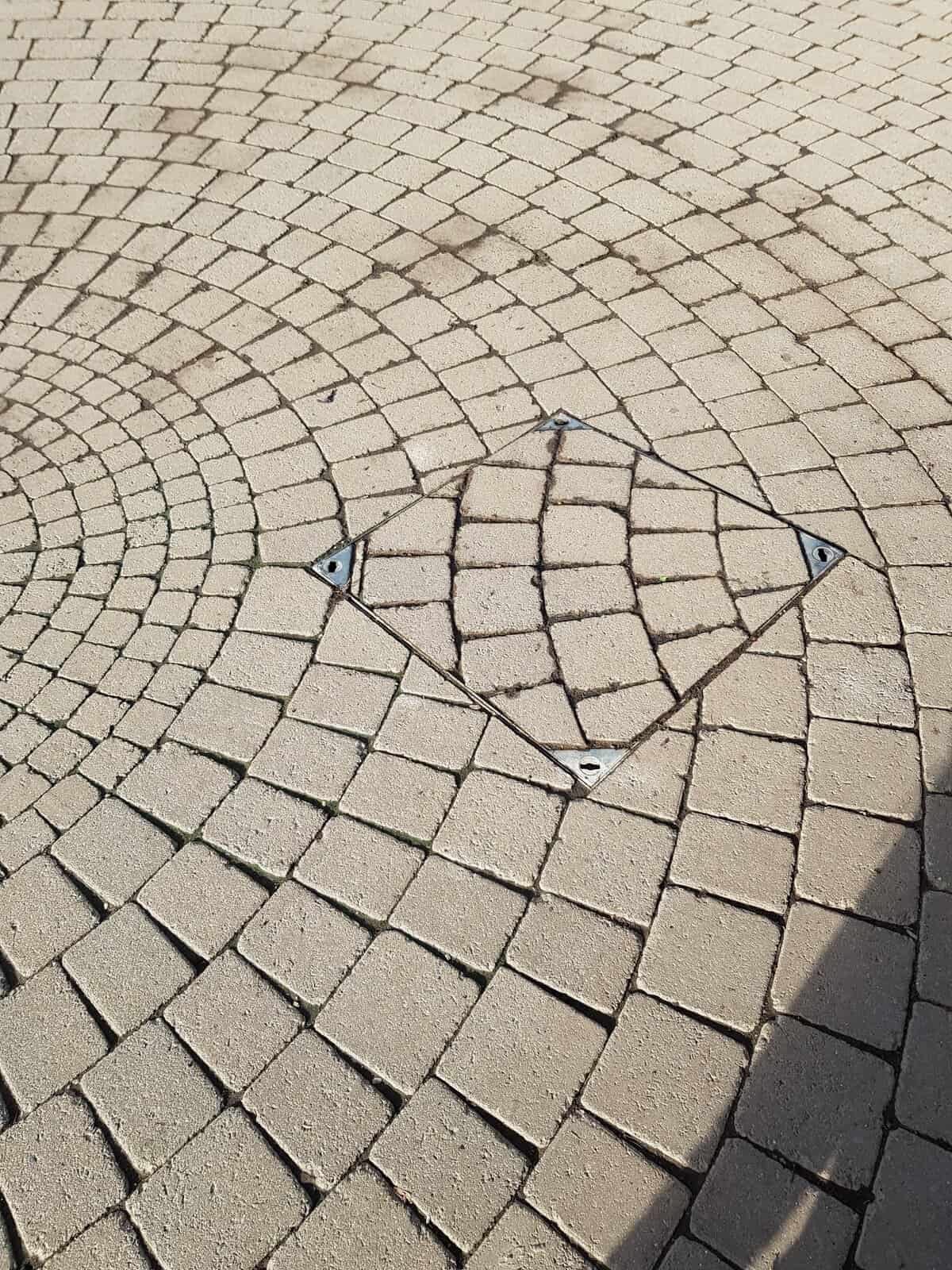 A frustrating "you had one job" fail showing a misaligned manhole cover on a cobblestone path.