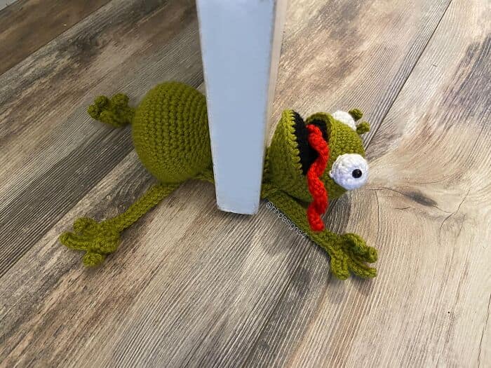 A funny and amazing crochet project of a frog being squashed under a door.