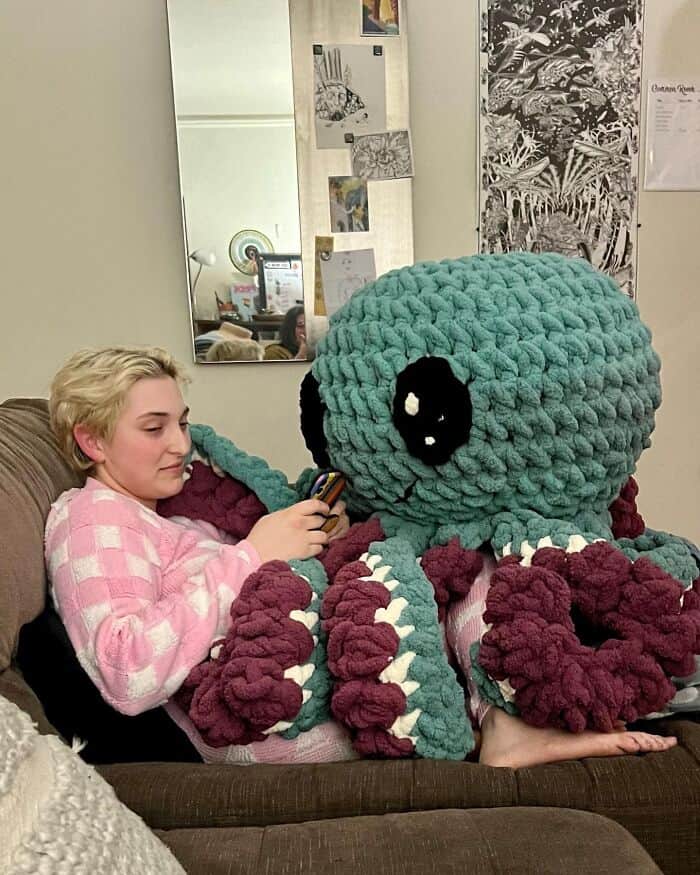 An amazing crochet plushie of a giant octopus sitting on a couch next to a person