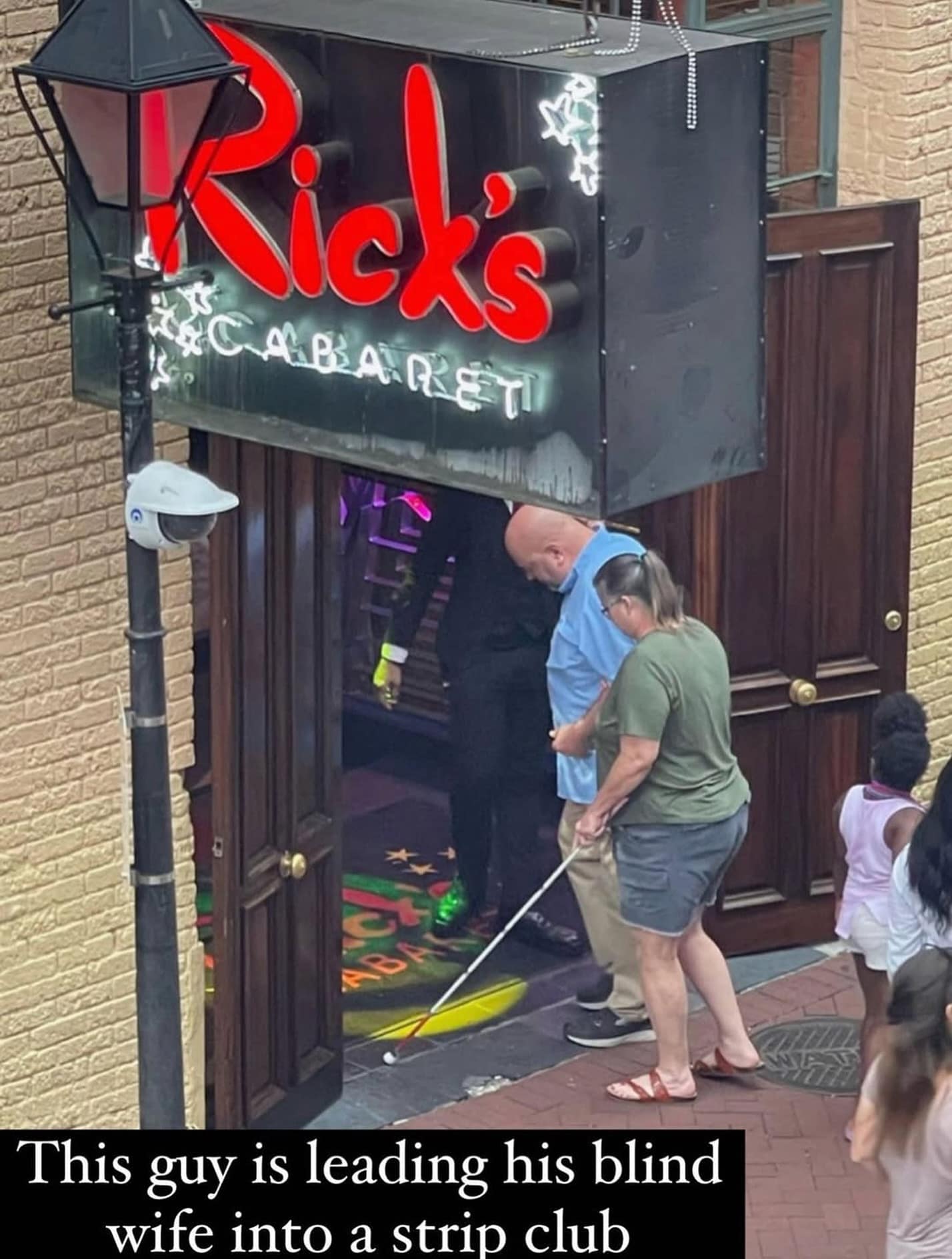 A funny meme showing a man leading his blind wife with a cane into a famous strip club.