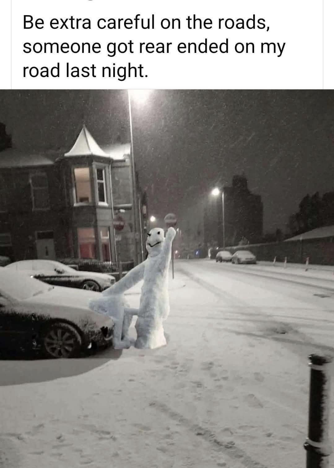 A funny and clever winter scene where a snowman has been built on the side of a road, posed as if it was just rear-ended by a car.