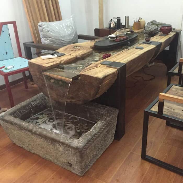 Rustic wooden table with a built-in water channel pouring into a stone basin inside a living room.
