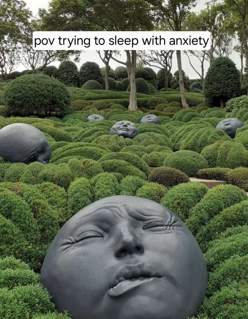 Garden of rounded shrubs with giant stone faces emerging; caption: “pov trying to sleep with anxiety.”