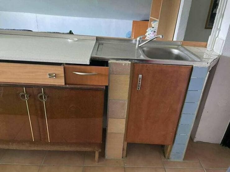 A bizarre and poorly constructed kitchen featuring a modern sink that has been installed on a combination of old cabinets and stacked tiles.