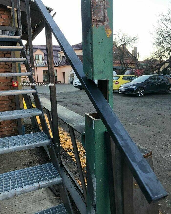 A poorly constructed outdoor metal staircase where the handrail has been incorrectly installed on the wrong side of the main support posts.