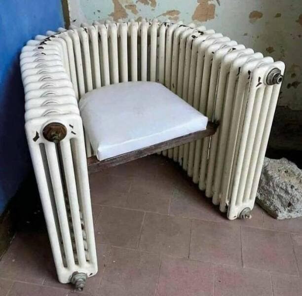 A unique and probably very hot or very cold chair that has been constructed by bending an old white cast-iron radiator into a U-shape.