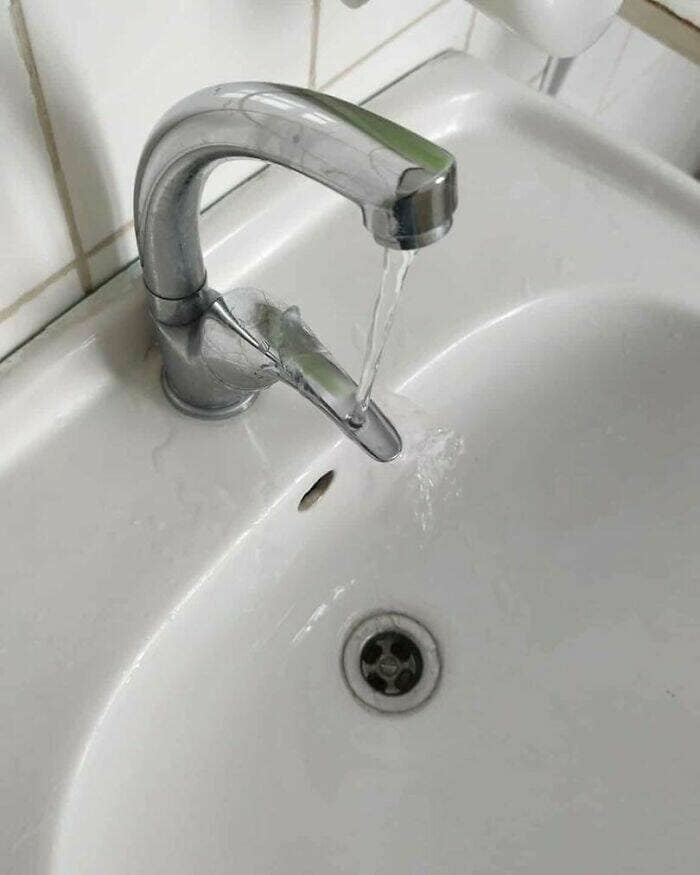 A broken bathroom sink faucet that has sprouted a second, smaller faucet from its side, with both spouts leaking water at the same time.