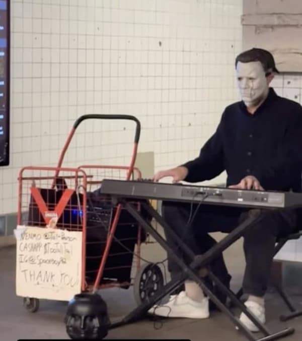 A funny photo of a man who is wearing a Michael Myers mask from the movie Halloween and is playing a keyboard in a subway station in order to entertain commuters and make some money.