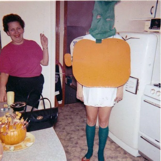 A funny and strange photograph from what appears to be a 1970s Halloween party, which shows a person wearing a very strange, abstract, and probably homemade pumpkin costume with a green ski mask.