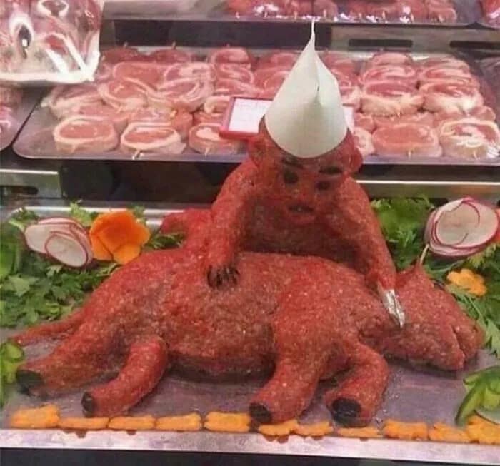 A cursed image from a butcher shop featuring a disturbing sculpture of a devil riding a dog, made of raw meat.