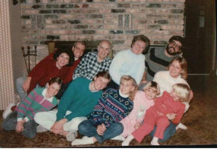 Awkward vintage large family photo featuring dated sweaters and one man sternly looking away from the camera.