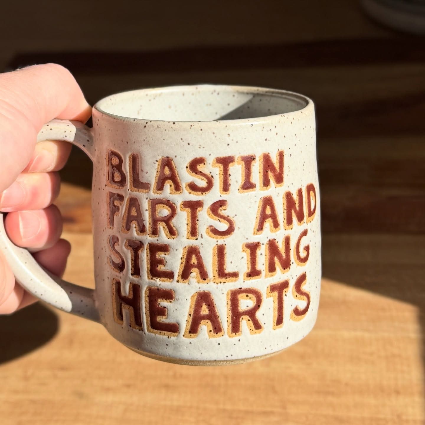 Funny memes picture of a handmade ceramic mug reading "Blastin farts and stealing hearts" in carved letters.