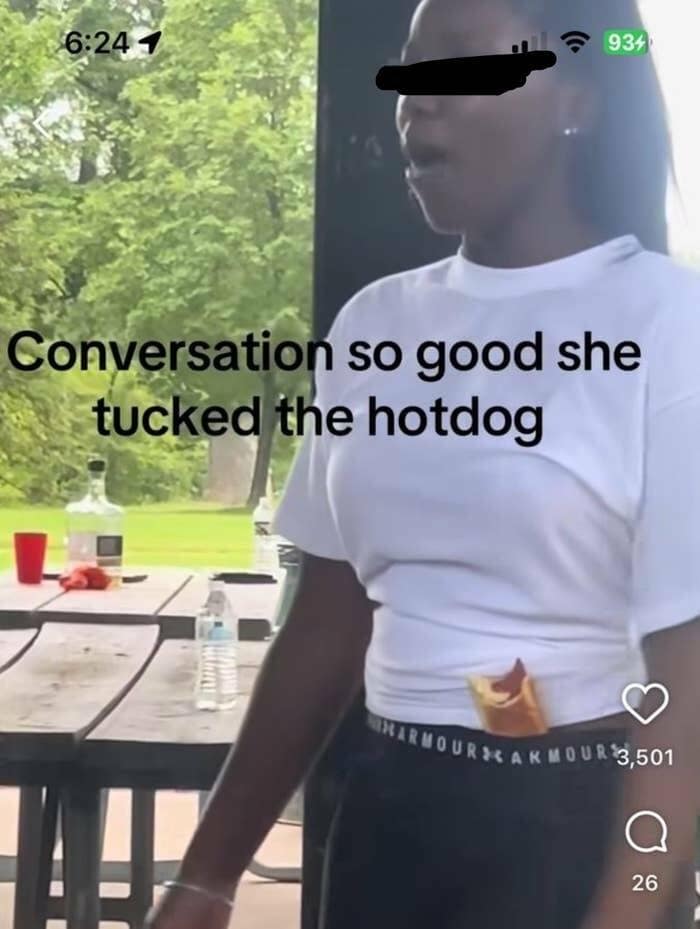 A funny meme photo of a woman who tucked her hotdog into her waistband mid-conversation.
