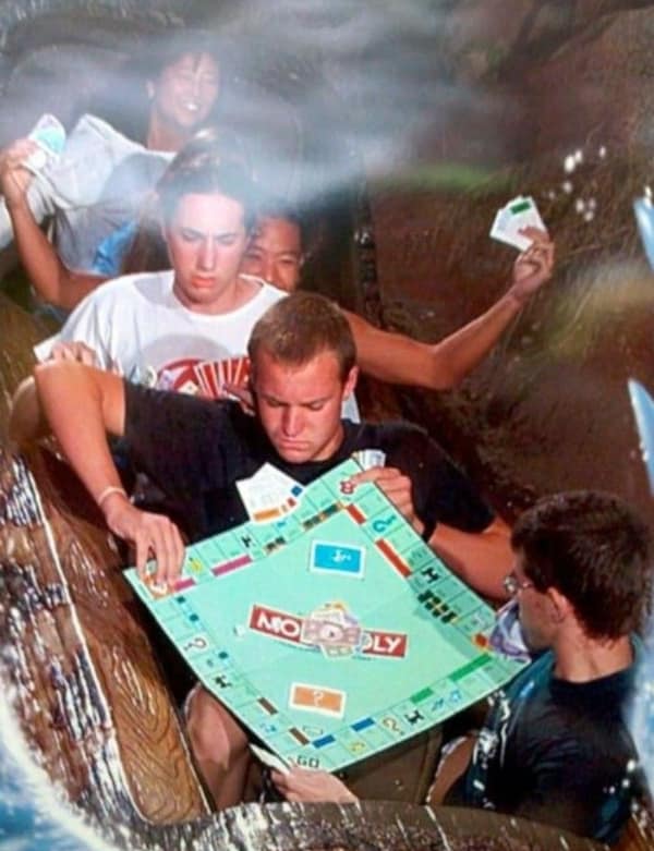 People intensely playing Monopoly board game while riding down a theme park log flume water ride.