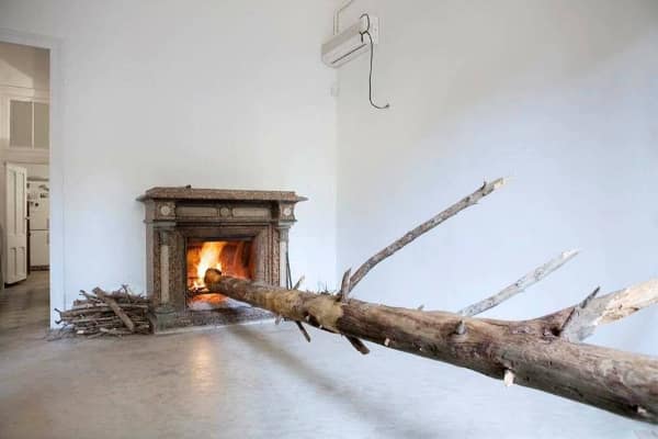A minimalist room featuring a fireplace with an absurdly long, entire tree log burning inefficiently inside it.