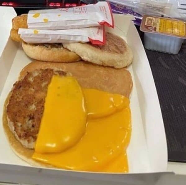 A photo of a poorly made McDonald's breakfast sandwich where the cheese is completely melted onto the cardboard box.