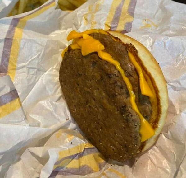 A photo of a sad and lonely-looking cheeseburger where the patty is hanging halfway off the bun.