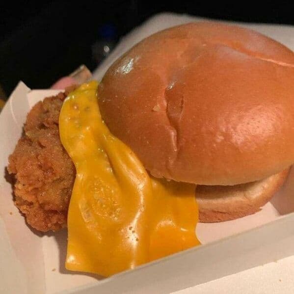 A photo of a chicken sandwich where the cheese has completely melted off the side and is dripping into the box.